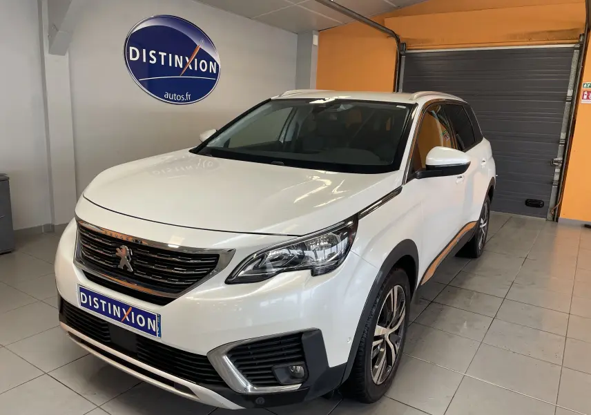Peugeot 5008 blanc nacré en 3/4 avant droit dans un showroom avec logo Distinxion en arrière-plan.