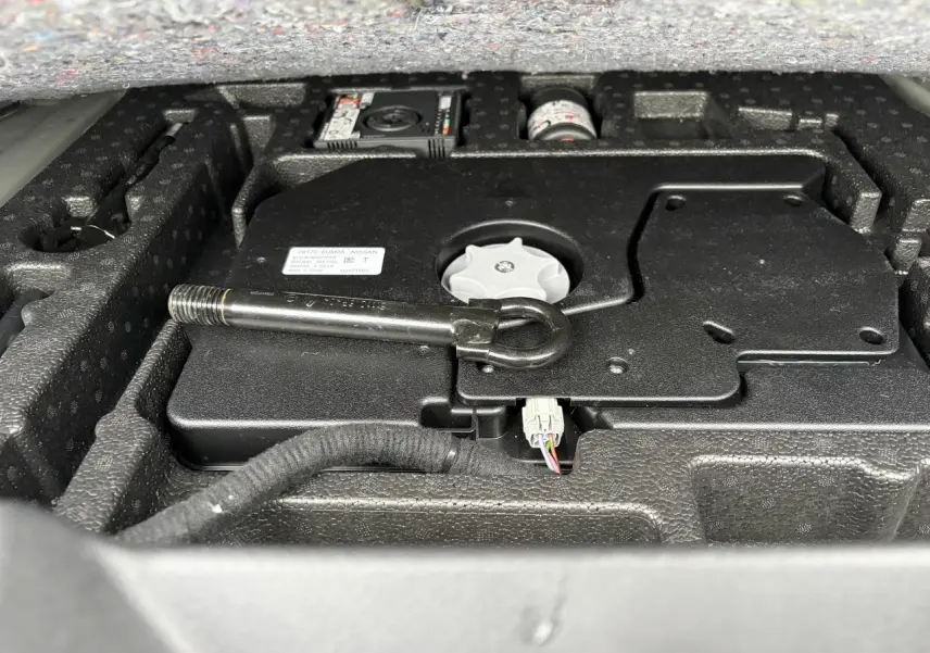 Gros plan sur le compartiment de rangement sous le plancher de coffre du Nissan Qashqai III, avec outil de remorquage visible.