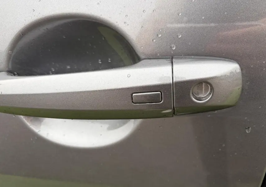 Poignée de porte avant droite couleur gris métallisé du Nissan Qashqai 2025 avec bouton d'ouverture mains libres et serrure visible.