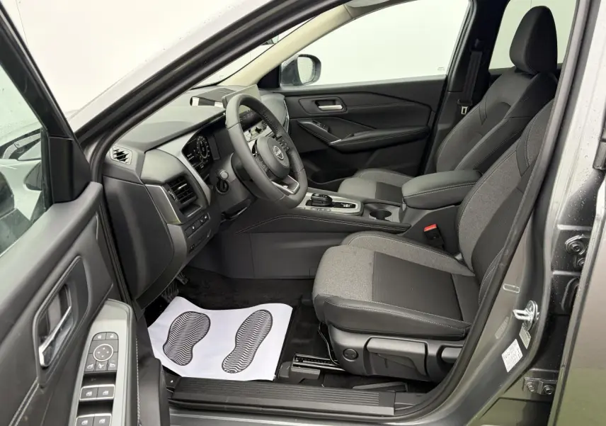 Vue intérieure côté conducteur du Nissan Qashqai III 2025 gris foncé, montrant sièges tissu et tableau de bord moderne.