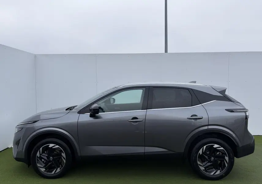 Profil droit du Nissan Qashqai III 1.5 Hybrid E-Power 2025 en gris métallisé avec jantes alliage noires et toit contrasté.