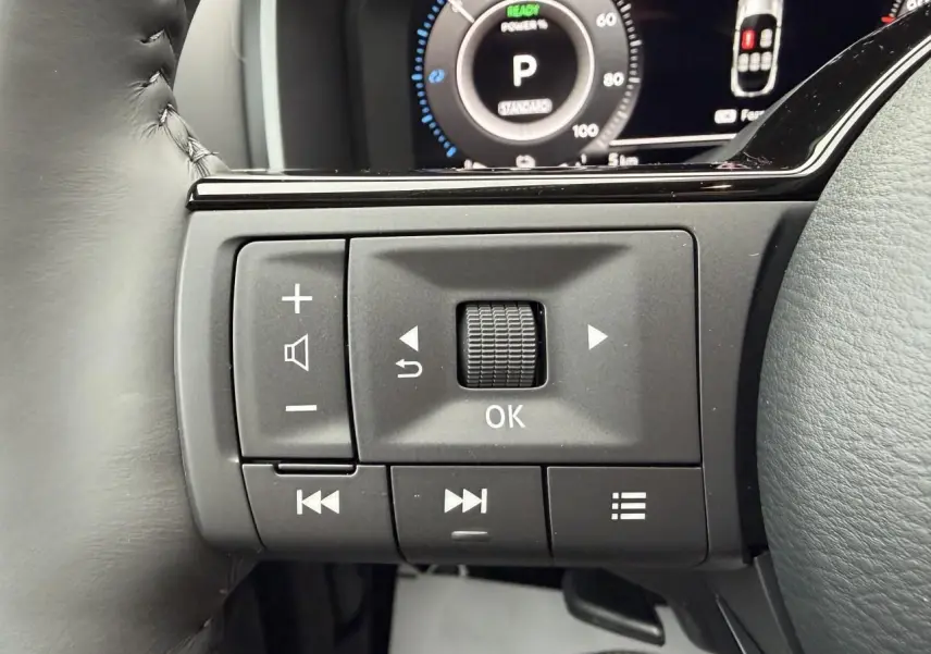 Gros plan sur les commandes multifonctions noires au volant du Nissan Qashqai III hybride, avec tableau de bord numérique en arrière-plan.