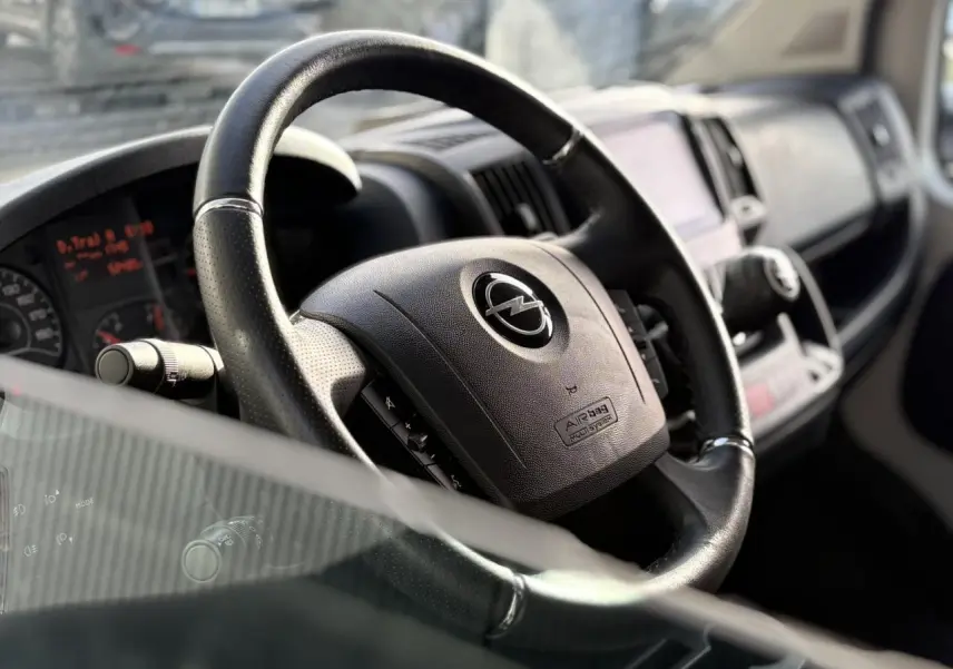 Gros plan sur le volant noir de l'Opel Movano Fourgon 2024, avec tableau de bord et écran tactile en arrière-plan.