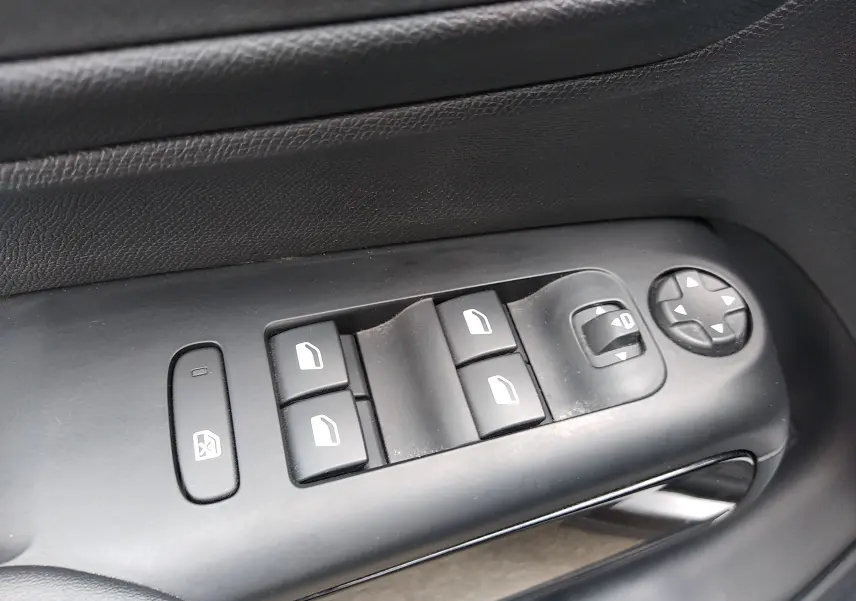 Gros plan sur les commandes de lève-vitres et réglages des rétroviseurs côté conducteur d’un Citroën C5 Aircross gris platinium.