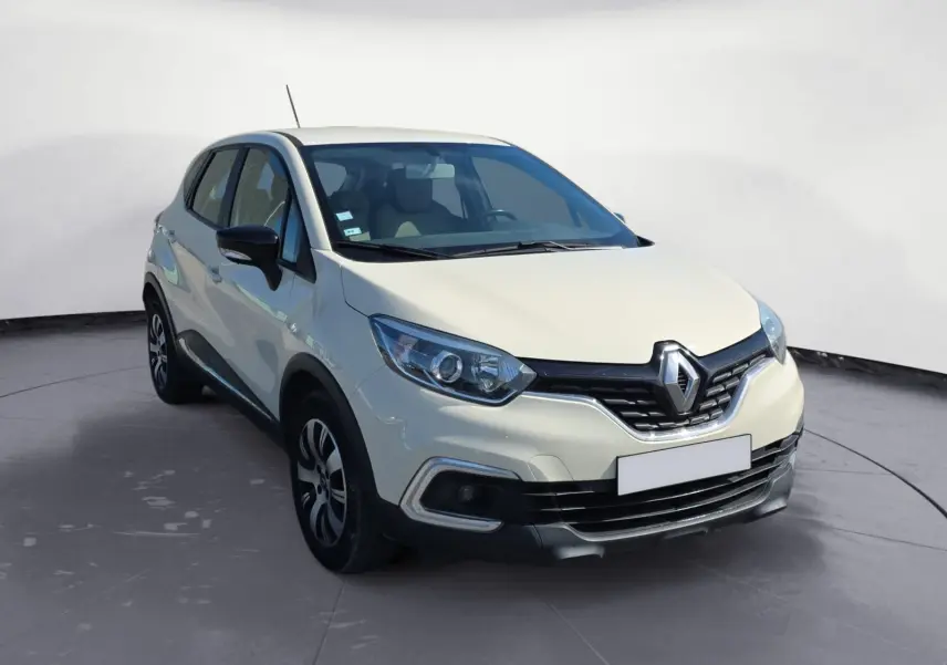 Profil droit d'un Renault Captur ivoire 2018 avec jantes alliage et protections noires sur un sol gravillonné.
