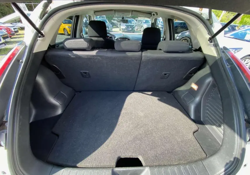 Coffre ouvert d’un Nissan Juke blanc, vue arrière montrant la banquette arrière et le plancher de coffre plat.
