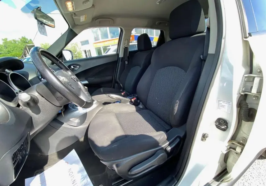 Vue intérieure côté conducteur du Nissan Juke blanc 2017, montrant les sièges avant en tissu noir et le volant multifonction.