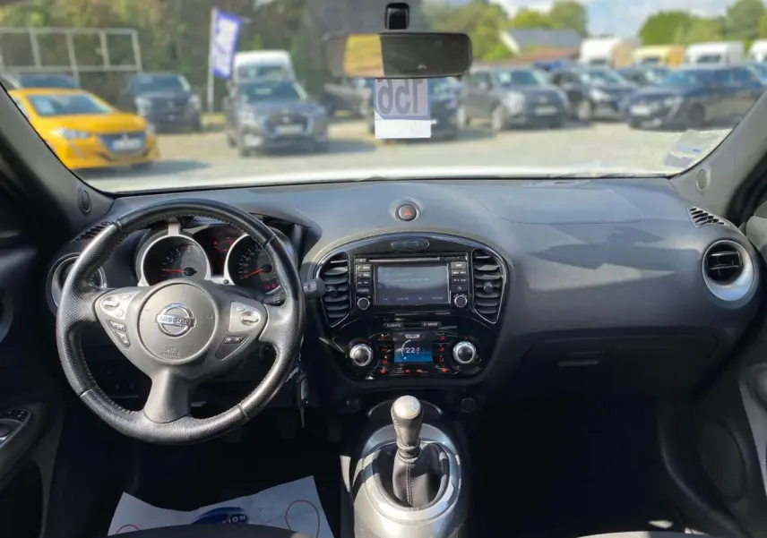 Vue intérieure du tableau de bord et volant d’un Nissan Juke blanc de 2017 avec boîte manuelle et écran central.