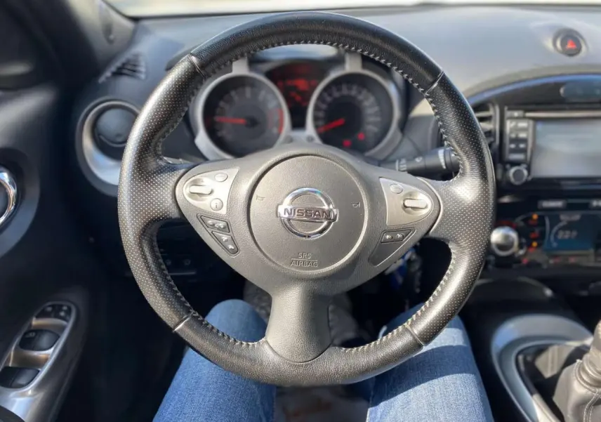 Vue intérieure centrée sur le volant noir perforé du Nissan Juke 2017 avec commandes intégrées et tableau de bord en arrière-plan.