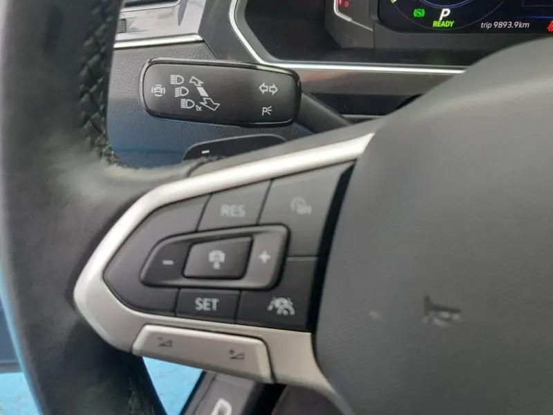 Gros plan sur les commandes multifonctions du volant cuir du Volkswagen Tiguan 1.4 eHybrid noir intense nacré, tableau de bord en arrière-plan.