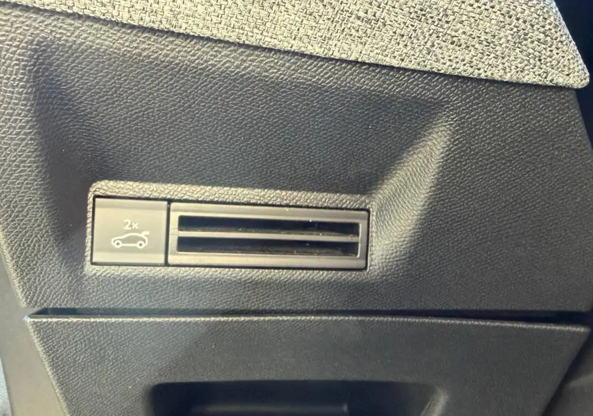 Détail du bouton d'ouverture électrique du coffre sur la console intérieure noire du Peugeot 5008 Hybrid blanc.
