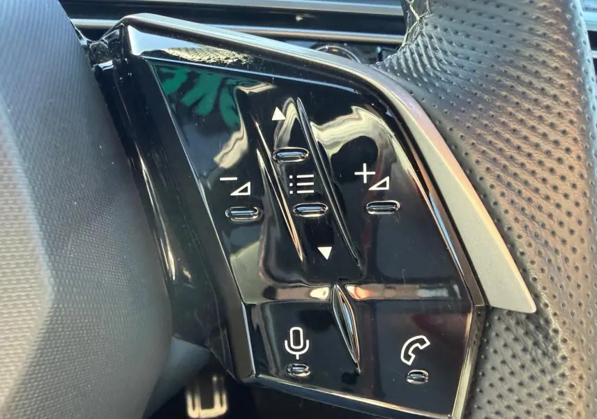 Gros plan sur les commandes noires du volant cuir perforé du Peugeot 5008 Hybrid blanc Okénite.