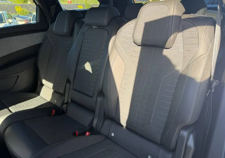 Vue rapprochée des sièges arrière noirs en tissu et cuir du Peugeot 5008 Hybrid 2025, avec appuis-tête et ceintures visibles.