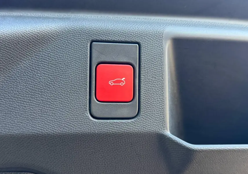 Gros plan sur le bouton rouge d'ouverture électrique du coffre du Peugeot 5008 Hybrid blanc Okénite.