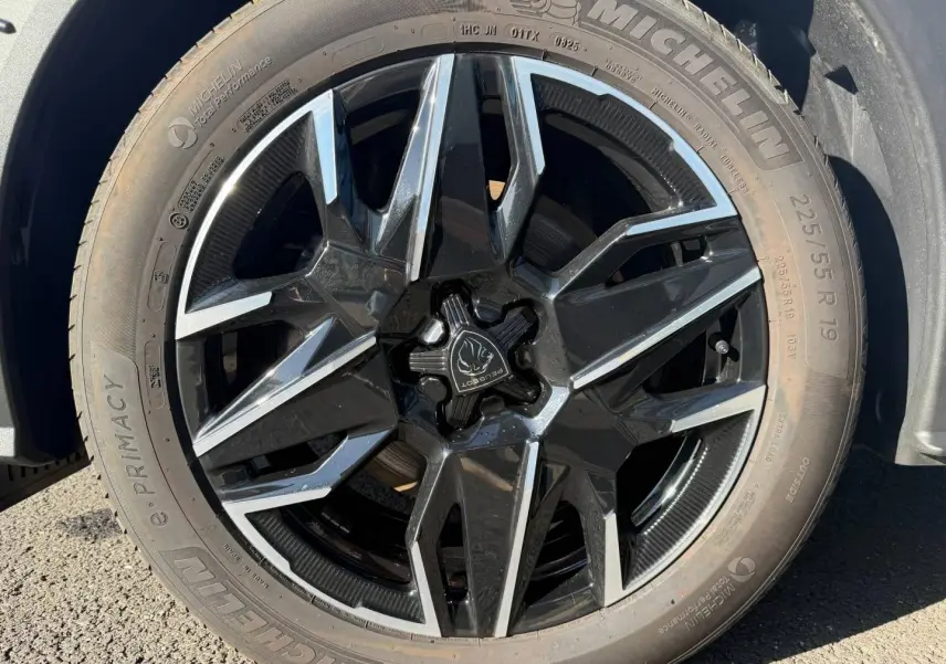 Gros plan sur la jante noire et argentée d’un Peugeot 5008 Hybrid blanc, avec pneu Michelin visible.