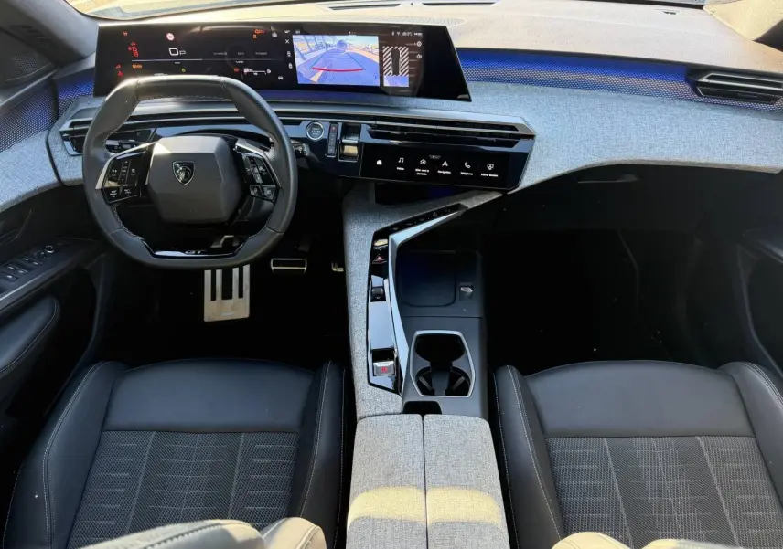 Vue intérieure avant du Peugeot 5008 Hybrid GT 2025, tableau de bord gris clair avec volant cuir noir multifonction et écran tactile large.