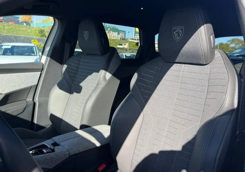 Vue intérieure sur les sièges avant gris tissu et cuir du Peugeot 5008 Hybrid 145ch GT, avec logo Peugeot brodé.