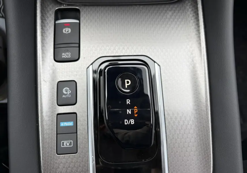 Gros plan sur la console centrale argentée et noire du Nissan Qashqai III 1.5 Hybrid avec sélecteur de boîte auto et boutons de fonctions.