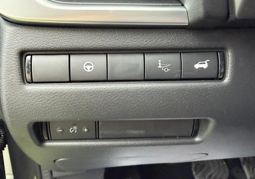 Gros plan sur les commandes intérieures noires du Nissan Qashqai 2025, côté conducteur, avec boutons de réglage et ouverture hayon.