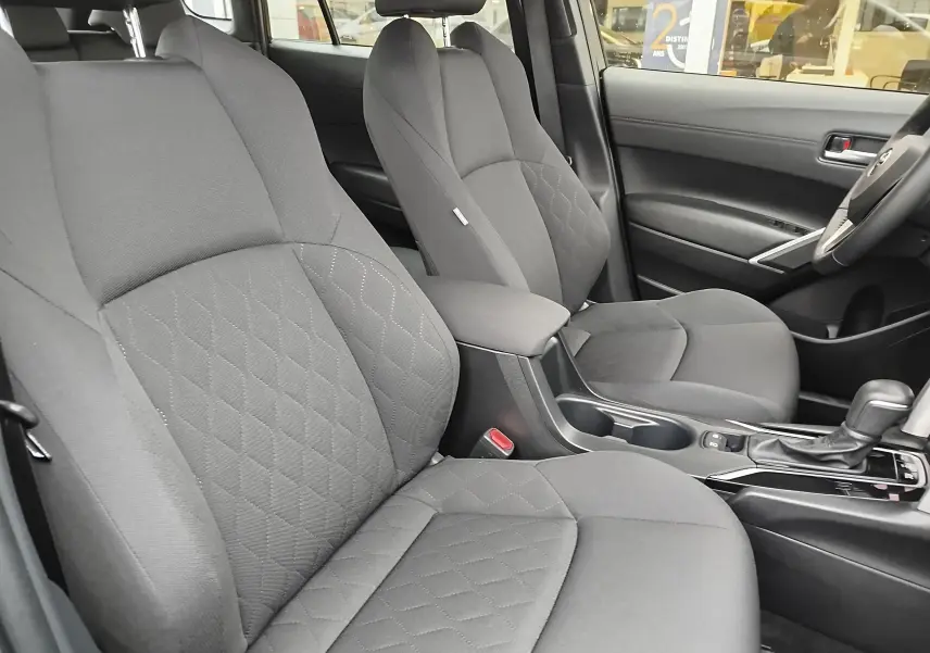 Vue intérieure côté droit du Toyota Corolla Cross 1.8 140ch Dynamic 2025, sièges tissu gris avec console centrale et levier de vitesse.