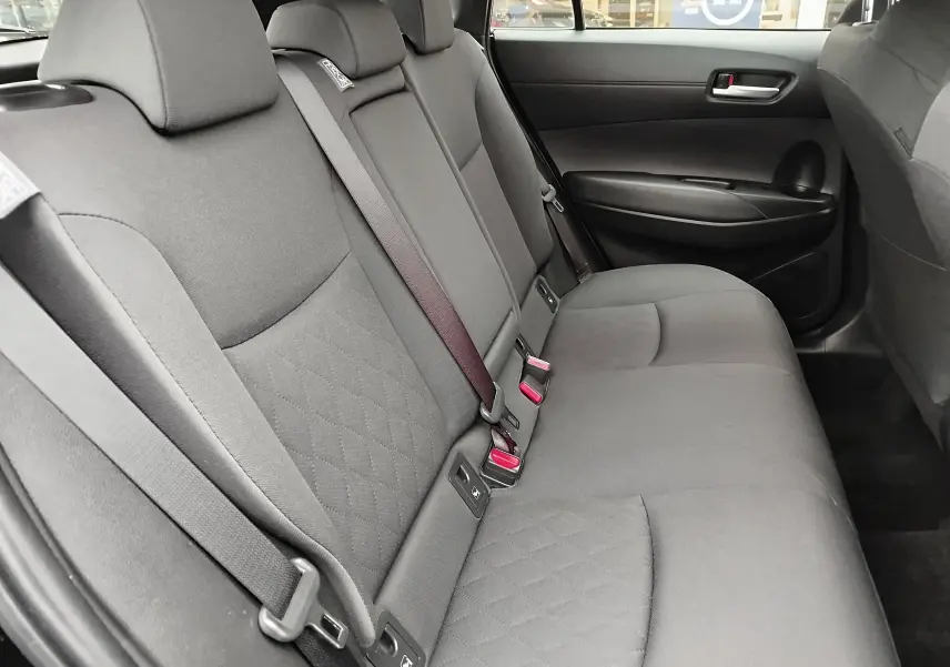 Vue intérieure du siège arrière côté droit de la Toyota Corolla Cross 2025, tissu gris avec ceinture de sécurité visible.