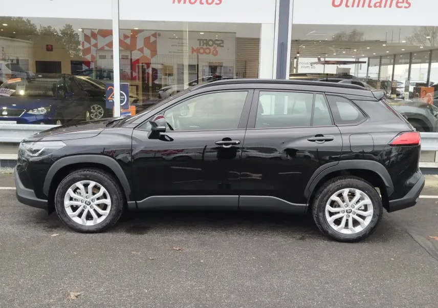 Vue de profil côté gauche d’un Toyota Corolla Cross 1.8 hybride noir intense, avec jantes alliage et protections noires.