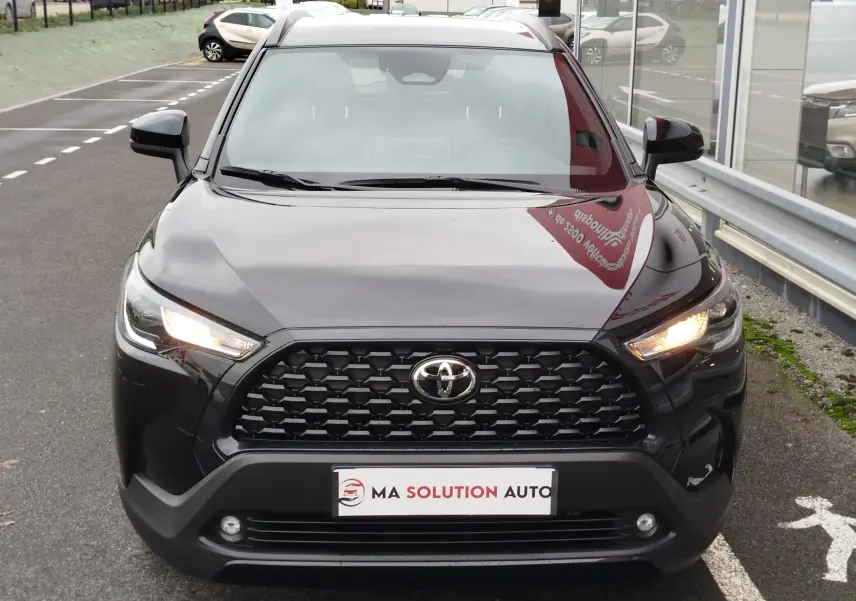 Vue avant d'une Toyota Corolla Cross 1.8 hybride noire intense avec calandre noire et feux allumés.