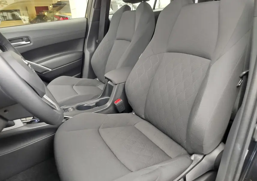 Vue intérieure côté gauche de la Toyota Corolla Cross 2025, sièges tissu gris avec motif losanges et accoudoir central.