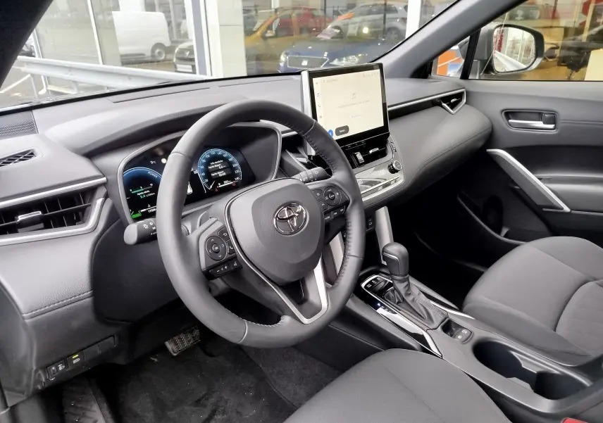 Vue intérieure côté conducteur du Toyota Corolla Cross 2025, tableau de bord moderne avec écran tactile central et volant multifonction noir.