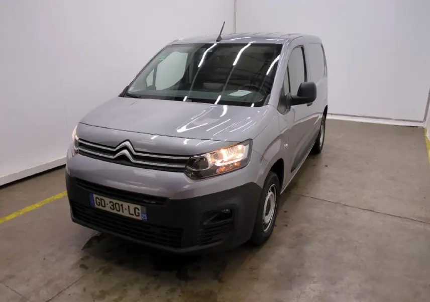 Vue 3/4 avant droit d'un Citroën Berlingo gris clair avec pare-chocs noirs et phares allumés dans un garage.