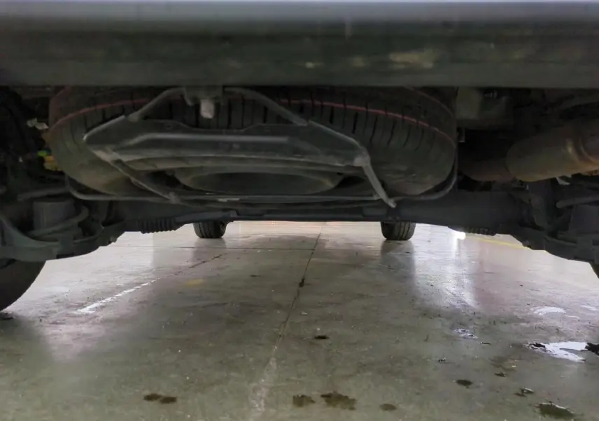 Vue en contre-plongée sous un Citroën Berlingo gris clair, montrant la roue de secours et le châssis.