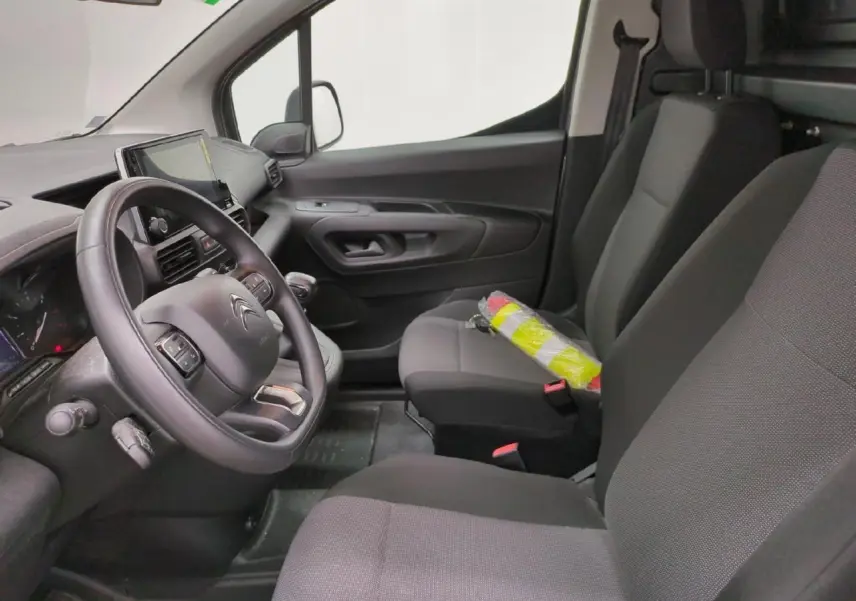 Vue intérieure côté conducteur du Citroën Berlingo gris clair, montrant le volant, la tablette tactile et les sièges tissu noirs.