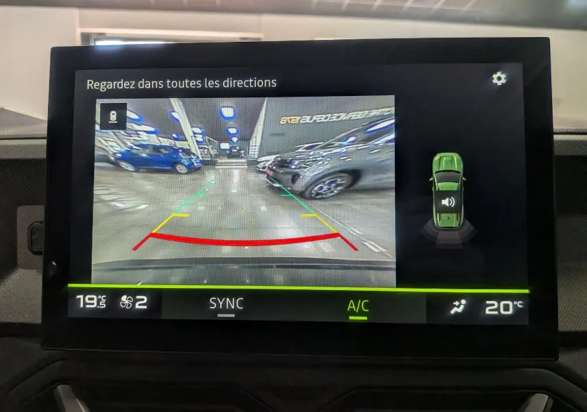 Écran de caméra de recul du Dacia Bigster vert cèdre montrant l'arrière avec lignes de guidage colorées en parking intérieur.