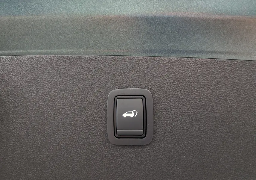 Bouton noir de commande d'ouverture du hayon sur tableau de bord en plastique texturé gris foncé du Dacia Bigster Vert Cèdre.