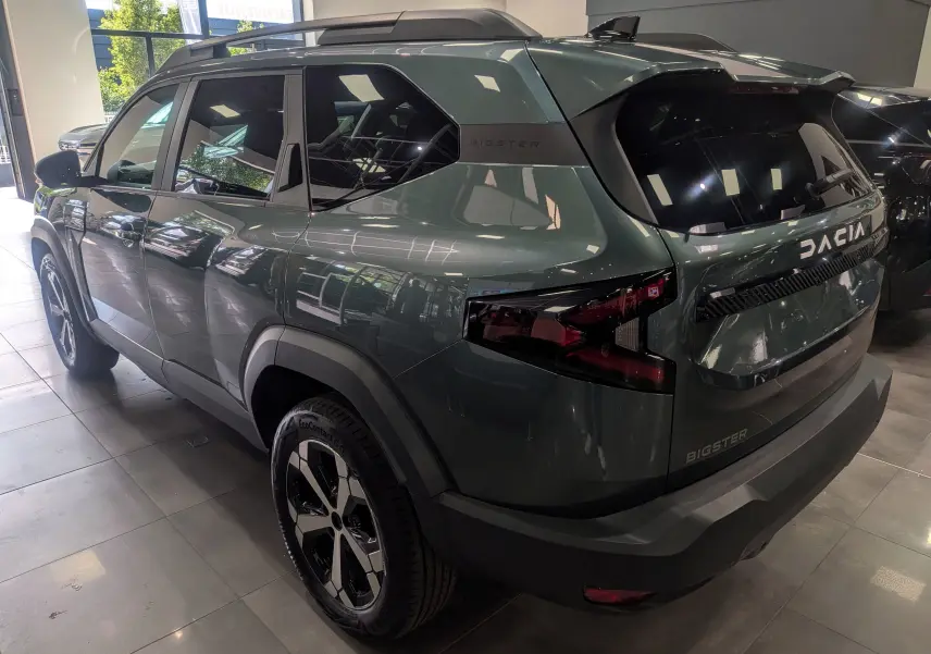 Vue 3/4 arrière droite du SUV Dacia Bigster vert cèdre avec jantes biton et feux arrière LED en showroom.