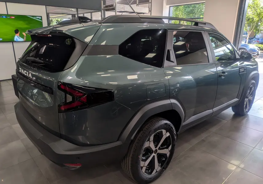 Vue 3/4 arrière droite du Dacia Bigster Vert Cèdre avec jantes noires et toit noir en showroom.