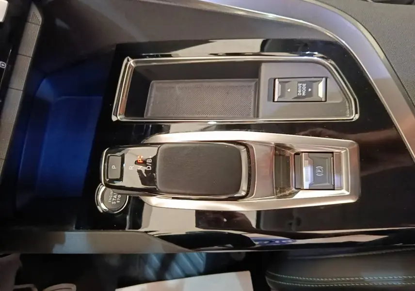 Vue rapprochée de la console centrale noire brillante du Peugeot 3008 1.6 HYBRID 225 avec levier de vitesses et bouton mode.
