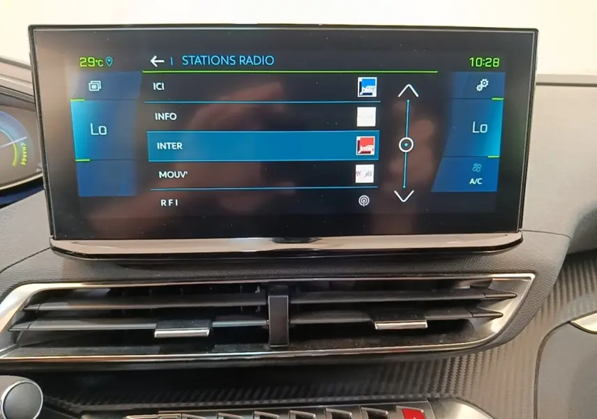 Écran tactile central affichant les stations radio dans l’habitacle du Peugeot 3008 hybride bleu, vue frontale rapprochée.