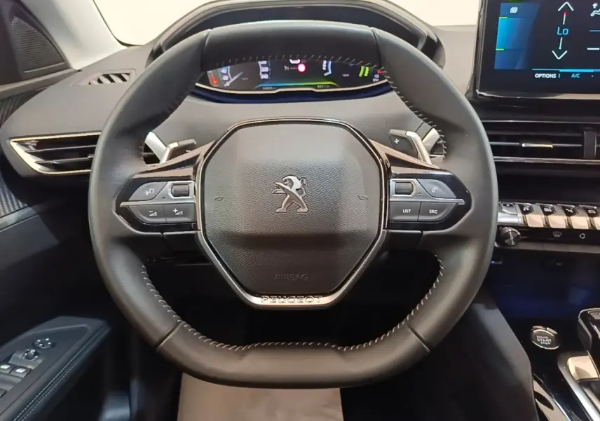 Vue rapprochée du volant cuir multifonctions noir du Peugeot 3008 1.6 Hybrid 225, avec tableau de bord digital en arrière-plan.