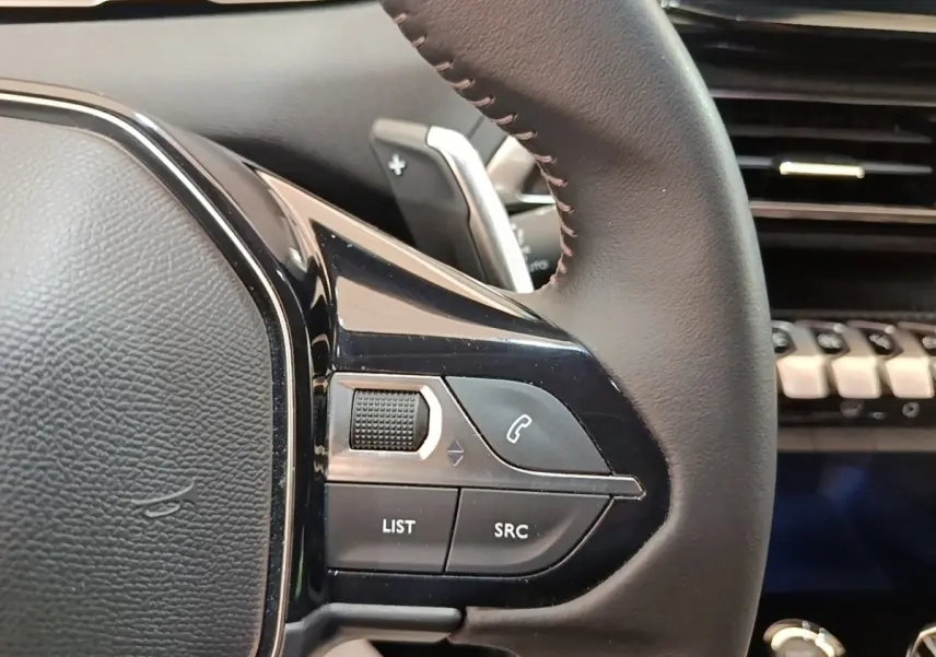 Gros plan sur le côté gauche du volant cuir noir du Peugeot 3008 hybride 2023 avec commandes multifonctions.