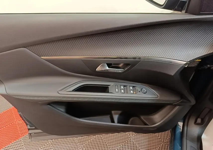 Intérieur côté gauche de la porte avant d’un Peugeot 3008 bleu, avec commandes électriques et finition carbone.