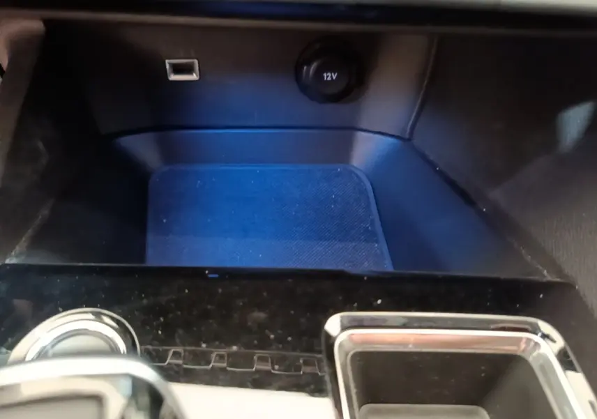 Gros plan sur la console centrale noire du Peugeot 3008 hybride 2023 avec prise 12V et port USB visible.