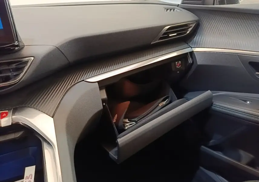 Intérieur du Peugeot 3008 hybride 2023, vue côté passager sur la boîte à gants ouverte et tableau de bord noir texturé.
