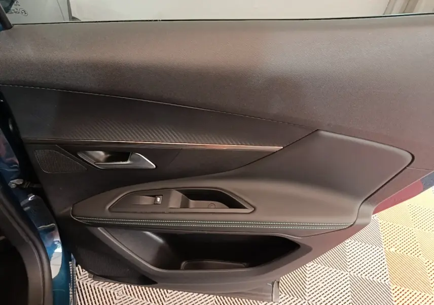 Vue rapprochée de la porte avant gauche bleu métallisé du Peugeot 3008 1.6 Hybrid avec garniture noire et surpiqûres blanches.