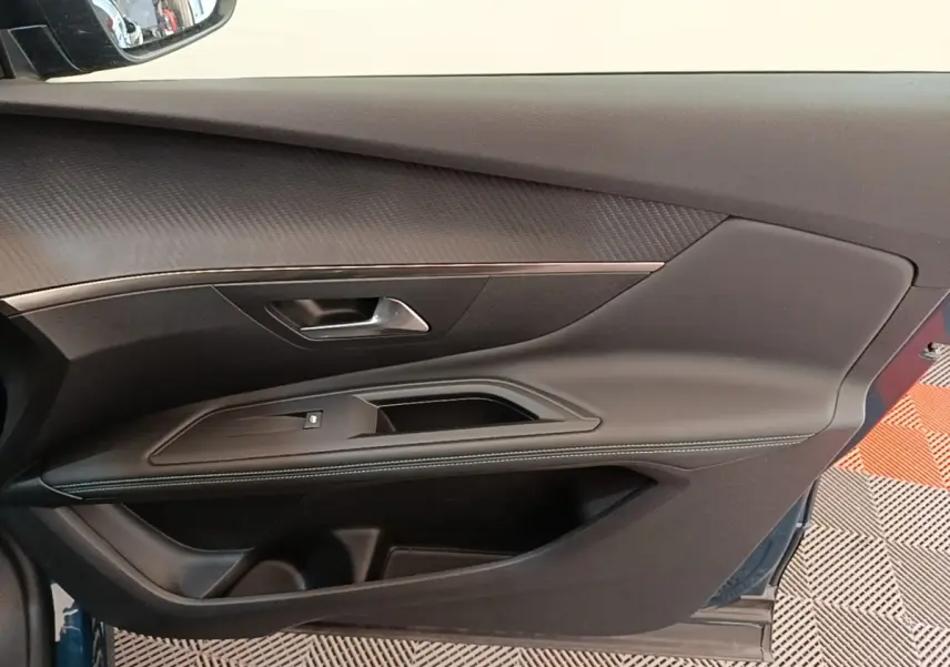 Vue rapprochée de la porte avant gauche du Peugeot 3008 bleu, avec garniture noire et surpiqûres blanches.