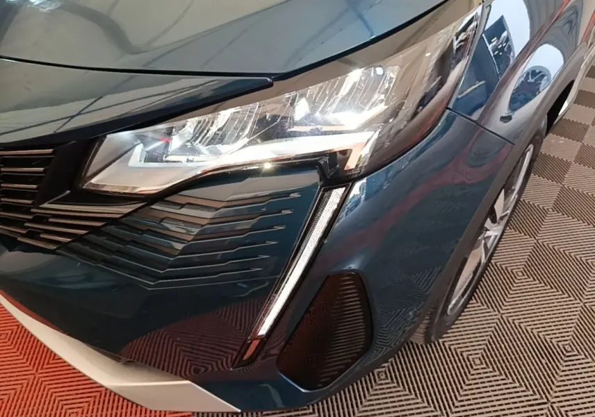 Gros plan sur l'avant droit bleu du Peugeot 3008 1.6 HYBRID 225 avec phare LED et calandre distinctive.