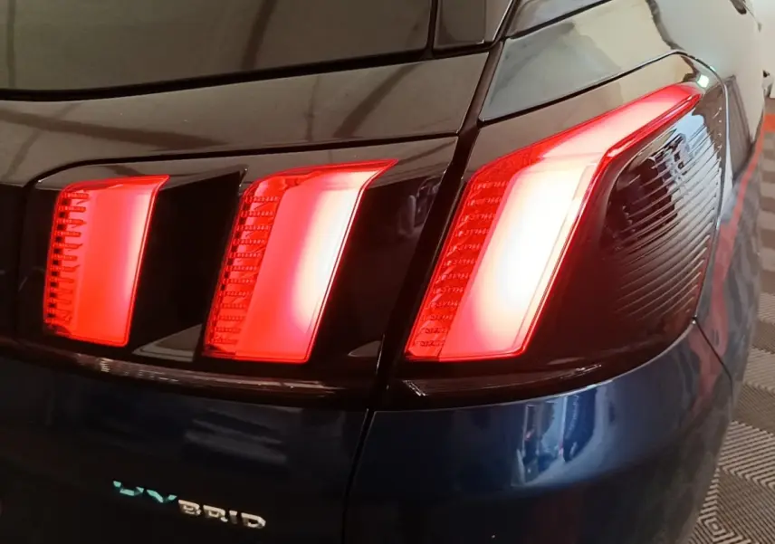 Gros plan sur le feu arrière droit rouge du Peugeot 3008 bleu hybride rechargeable, avec logo HYBRID visible.