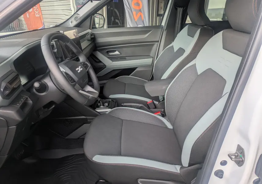 Vue intérieure côté conducteur du Dacia Duster Hybrid 155 Extreme blanc glacier, sièges tissu bicolore avec logo embossé.