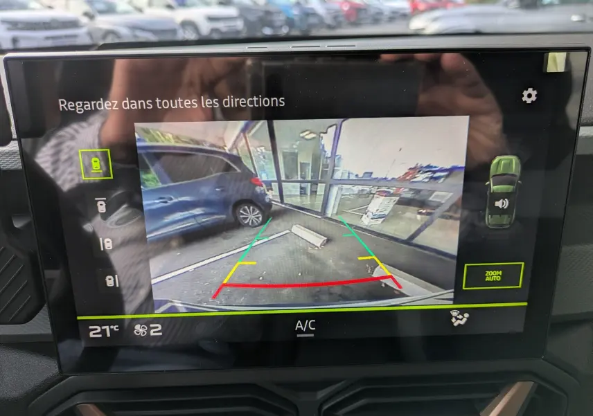 Écran intérieur montrant la caméra de recul du Dacia Duster blanc glacier, avec guidage de trajectoire coloré.