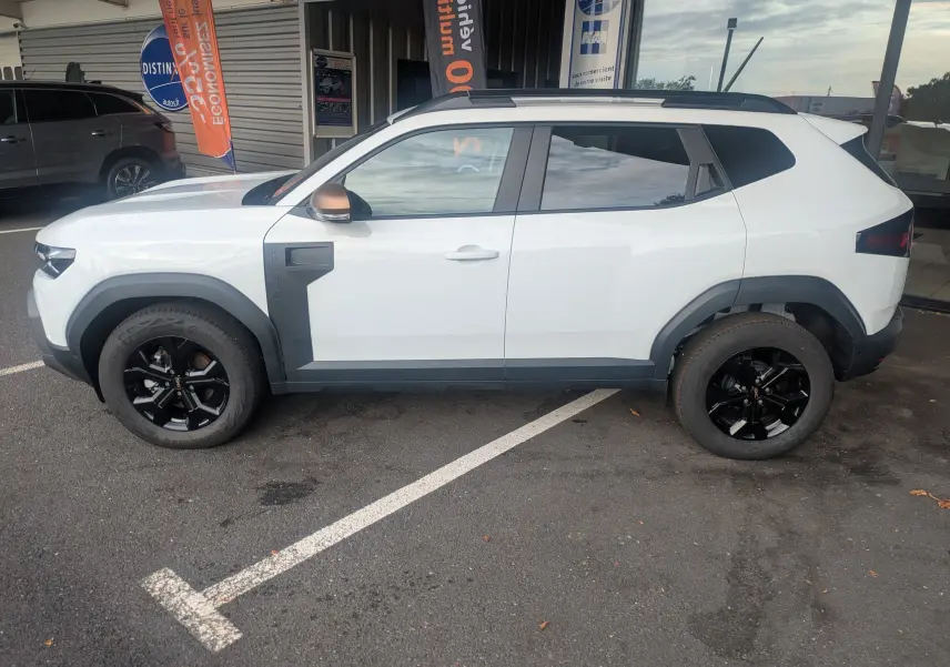 Vue de profil côté gauche du Dacia Duster Hybrid 155 Extreme blanc glacier avec jantes noires et coques de rétroviseurs brun cuivré.